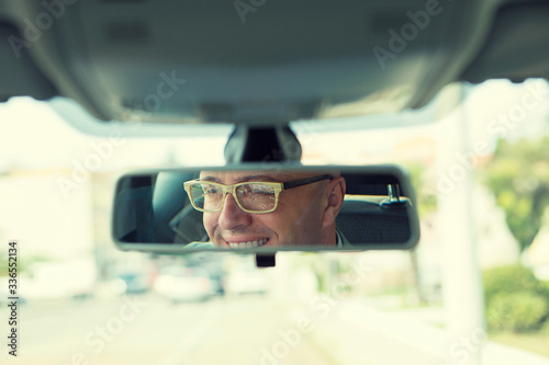 Happy with my car choice. Portrait young man driver reflection in car rear view mirror.