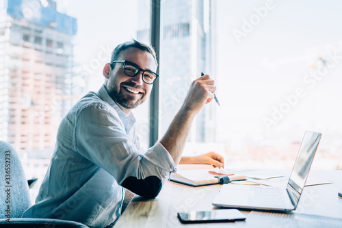 Fotografiet Portrait of cheerful male entrepreneur in classic eyewear smiling at camera whil