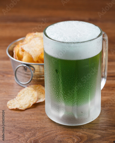 Cerveja verde de saint Patrick em caneca gelada com chips de batatas fritas sobre mesa de madeira photo