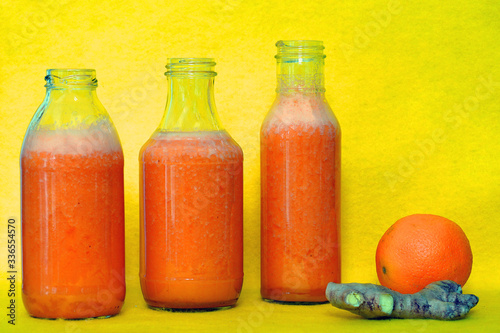 Glass bottles filled with colorful fresh homemade orange  carrot and ginger smoothies