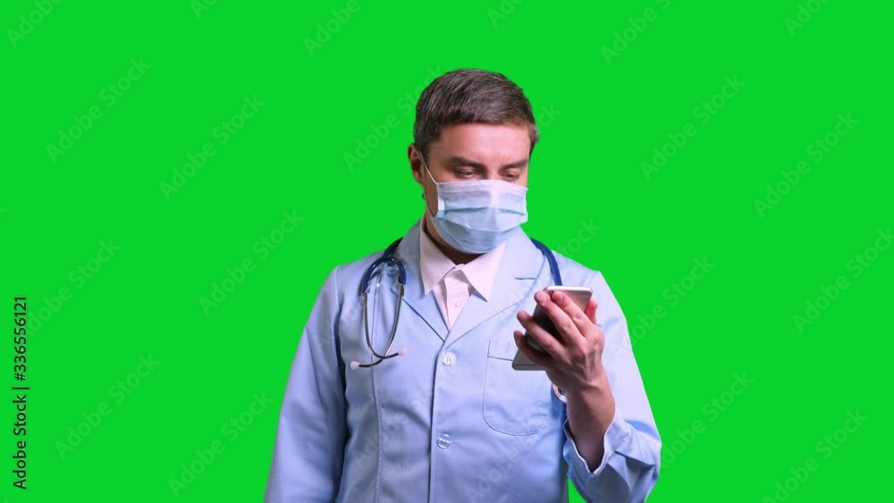 Young doctor using smartphone. Man in blue medical uniform with stethoscope on green chroma key background Young doctor using smartphone. Man in blue medical uniform with stethoscope on green chroma key background