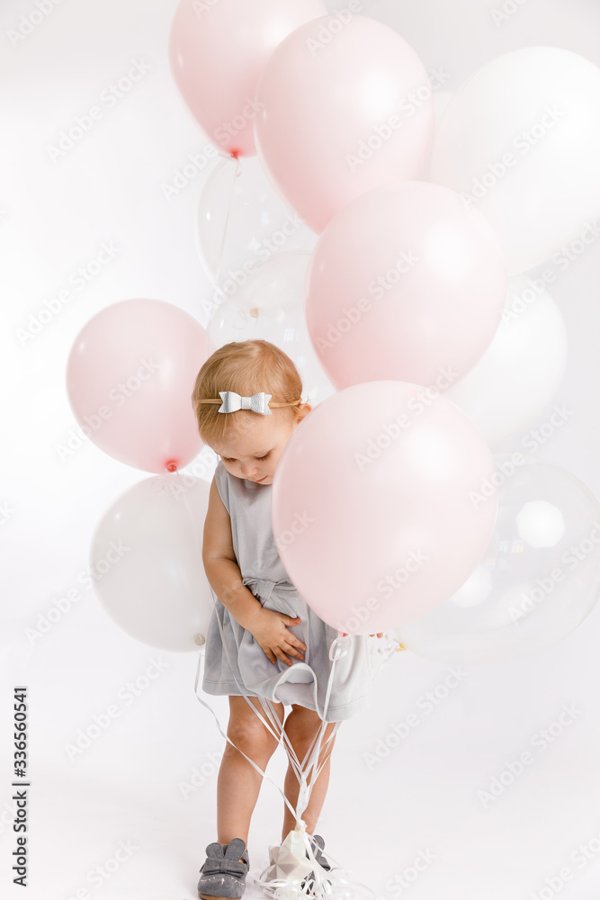 Little cute girl got tangled in a bunch of pink and white balloons enjoy festive birthday event wear grey pastel summer dress rabbit-footwear isolated on a white background. Little cute girl got tangled in a bunch of pink and white balloons enjoy festive birthday event wear grey pastel summer dress rabbit-footwear isolated on a white background.