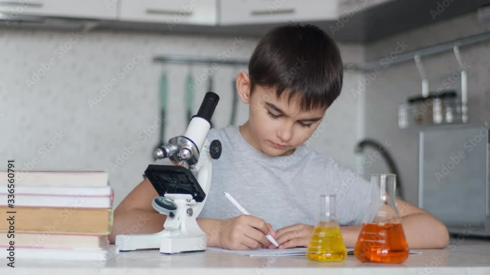 A boy learns chemistry using a microscope and makes notes in a notebook. Homework A boy learns chemistry using a microscope and makes notes in a notebook. Homework