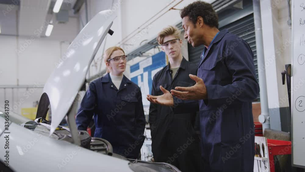Male tutor looking at car engine with students studying auto mechanic apprenticeship at college - shot in slow motion Male tutor looking at car engine with students studying auto mechanic apprenticeship at college - shot in slow motion