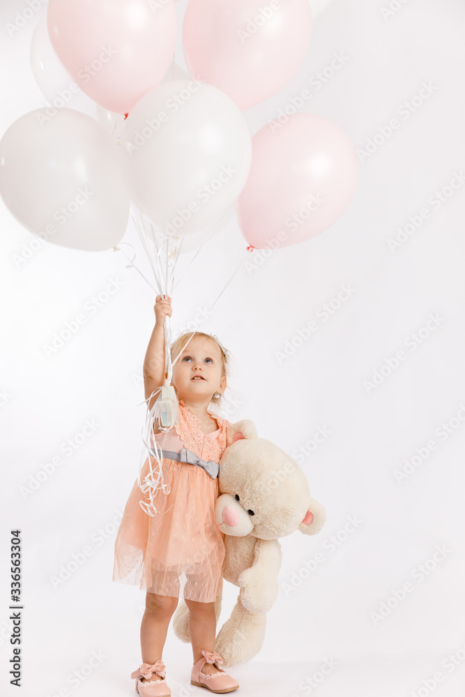 Little cute girl holds branch of balloons and large Teddy bear enjoy festive birthday event wear pink pastel summer dress isolated on a white background. Little cute girl holds branch of balloons and large Teddy bear enjoy festive birthday event wear pink pastel summer dress isolated on a white background.