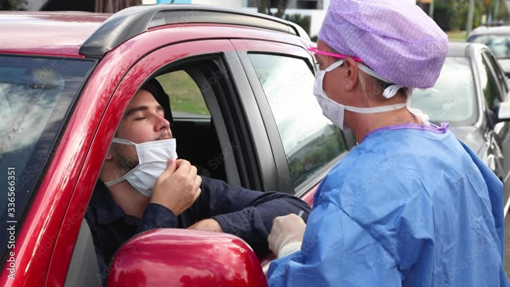 A doctor in a protective suit taking a nasal swab from a driver to test for possible coronavirus infection