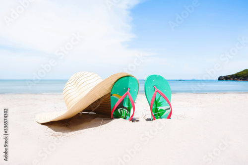 Green flip-flops embroidered on the sand and the hat at the sea with space of blue sky summer holiday and vacation concept.