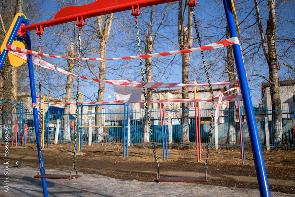 Fototapeta premium Childrens swing is wrapped in police tape. Concept of restriction of access, quarantine in connection with the pandemic of the COVID-19 virus.