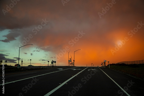 Intersection with black road and storm front with deep orange sky