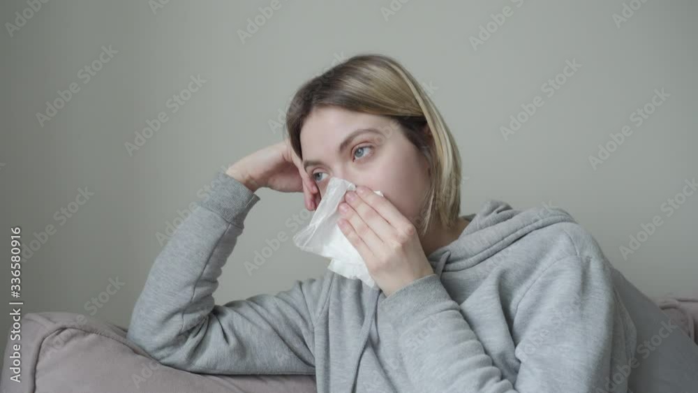 Close-up. The blonde girl with short hair is sick, sneezes and wraps herself in a blanket from the temperature. Symptom of Orvi, coronovirus, flu, acute respiratory disease, allergy, sinusitis. Close-up. The blonde girl with short hair is sick, sneezes and wraps herself in a blanket from the temperature. Symptom of Orvi, coronovirus, flu, acute respiratory disease, allergy, sinusitis.