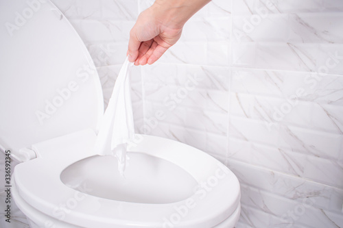 Close up hand throwing toilet paper to the toilet in a white tile bathroom