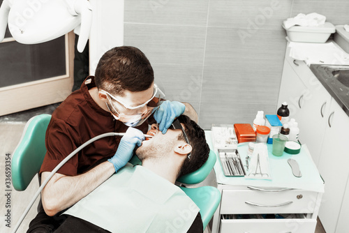 A young male dentist doctor treats a patient. Medical manipulations in dentistry  surgery. Professional uniform and equipment of a dentist. Healthcare Equipping a doctor   s workplace. Dentistry