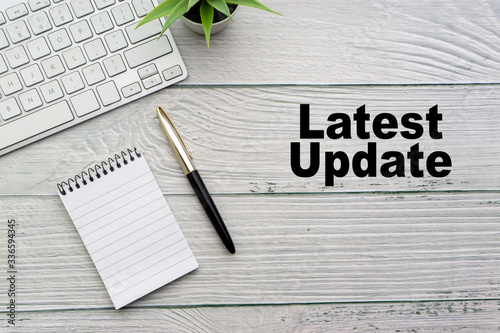 LATEST UPDATE text with notepad, keyboard, decorative vase and fountain pen on wooden background. Business and copy space concept