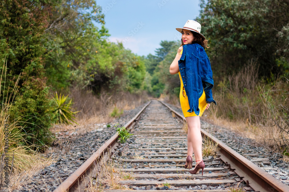 Rear view of a real woman walking on the railroad track, wearing yellow dress and hat