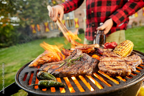 Slika na platnu Man holding a beer grilling meat on a BBQ