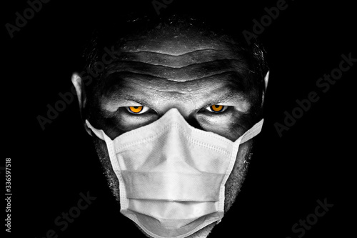 Dark and moody portrait of serious looking male adult with orange eyes wearing sugical maks for protection from Coronavirus or COVID-19