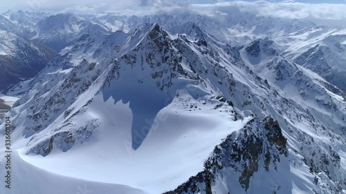 Helicopter flight over incredible epic mountain landscape winter snow covered sharp peaks of many rocky volcanic slopes. Mountains tops. Fairy nature Scandinavia Himalayas Tibet. Cumulus clouds sunny.