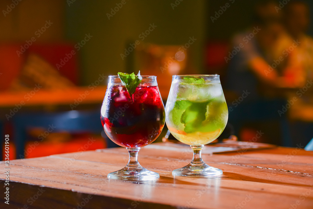 Two colorful refreshing cocktails served on a dark rustic wooden table with blurred background. Two colorful refreshing cocktails served on a dark rustic wooden table with blurred background.
