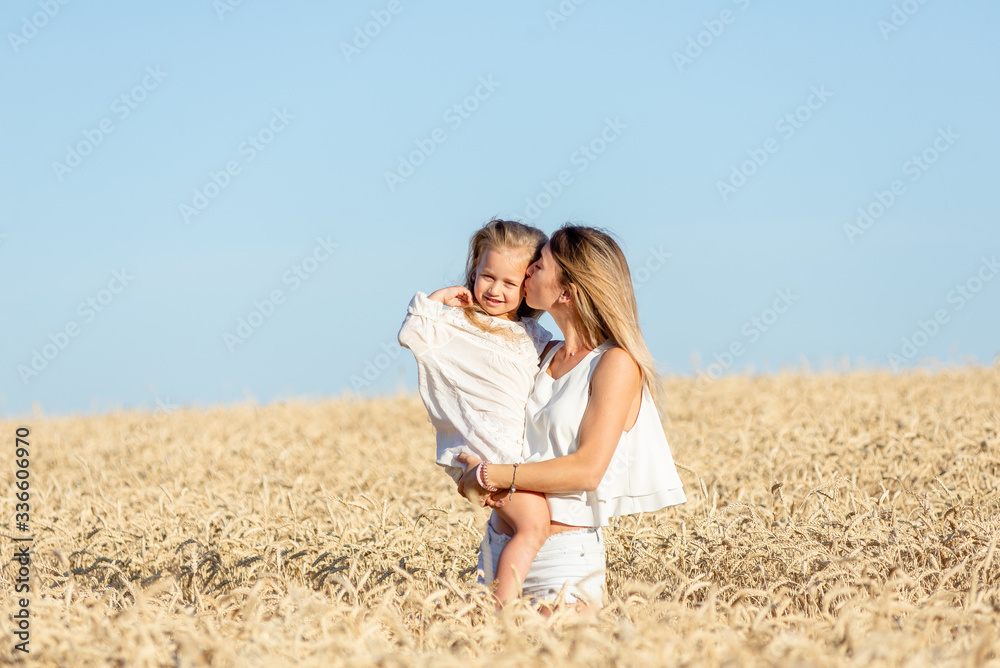 A young woman stands in a wheat field in the summer and holds her little daughter in her arms. A young woman stands in a wheat field in the summer and holds her little daughter in her arms.