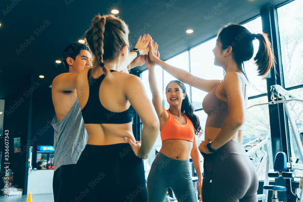Smile man and women making hands together in fitness gym. Group of young  people doing high five gesture in gym after workout. Happy successful  workout class after training. Teamwork concept Stock Photo