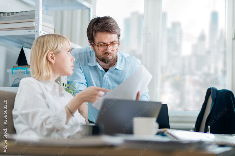 Kind manager giving feedback to young female intern in a busy downtown office. New employee asking for guidance on current project. Kind manager giving feedback to young female intern in a busy downtown office. New employee asking for guidance on current project.