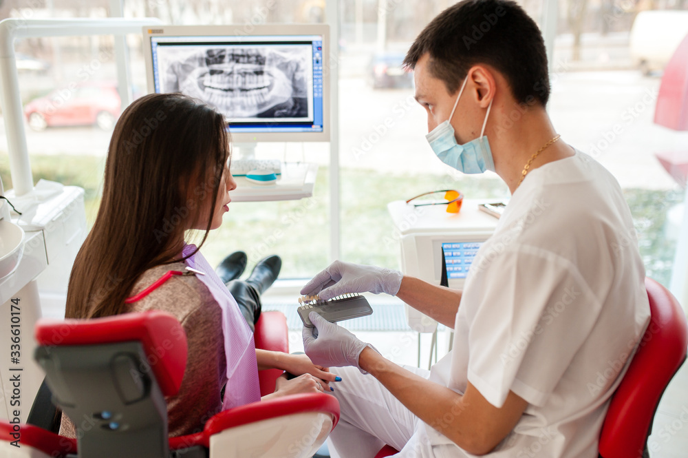 Choice of tooth color with a special scale. A dentist and an assistant select a shade of tooth enamel for the young pretty girl of the patient. Bleaching, prosthetics, orthopedic dentistry.