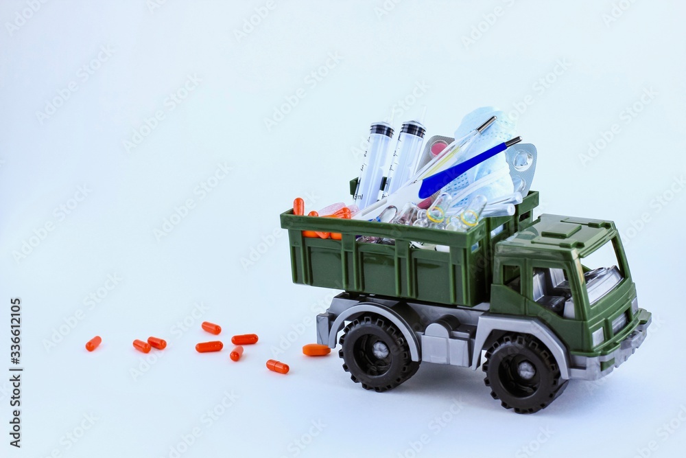 Fototapeta premium Military toy car with pills, medical masks, syringes and ampoules on light background. Concept of humanitarian aid, health care. Space for text.