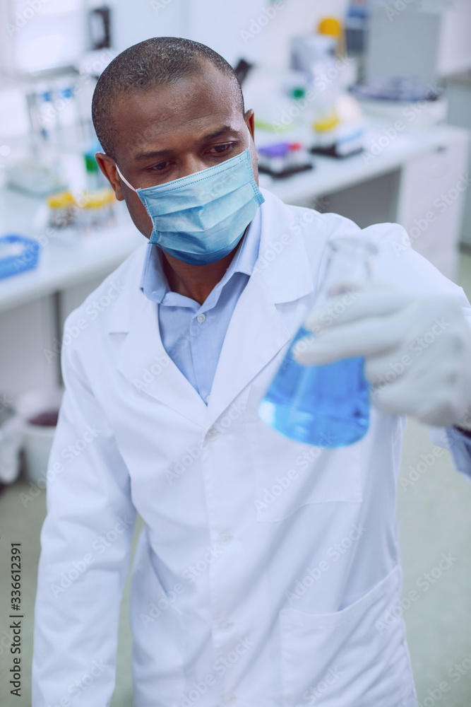 Concentrated male researcher looking at the flask Concentrated male researcher looking at the flask