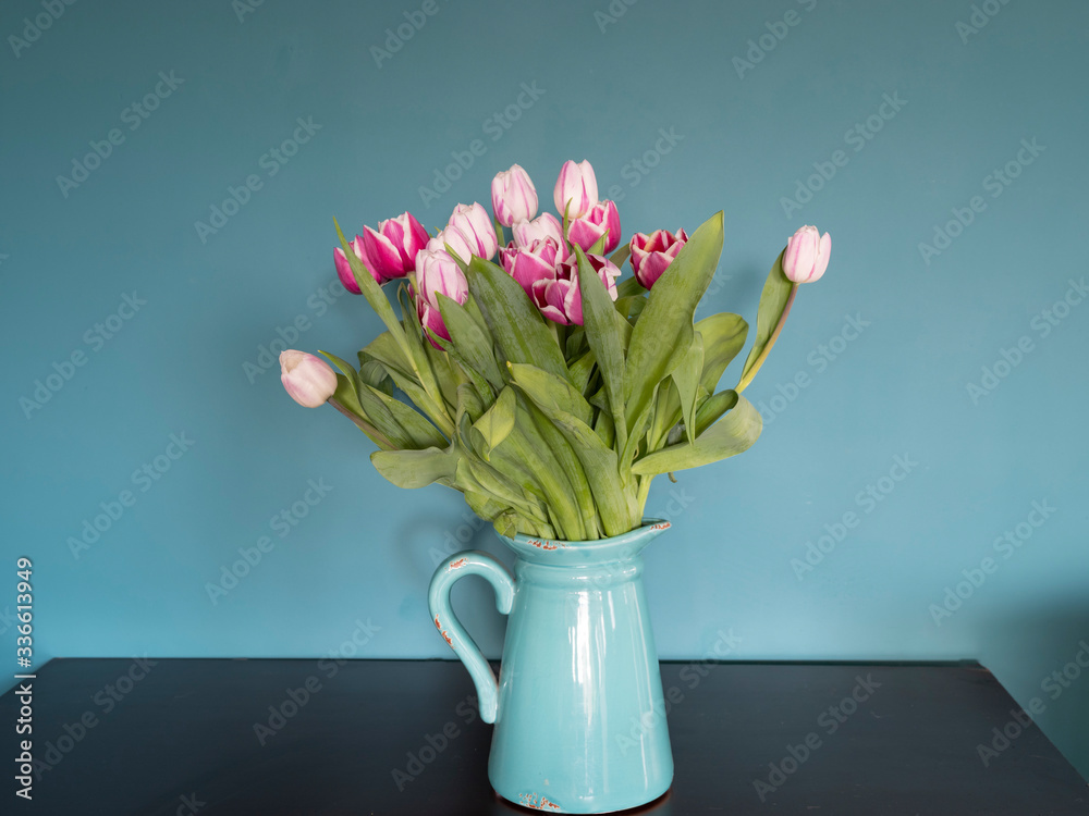 Fresh pink and red tulip flowers bouquet in a jug on a brown table in front of green wall. View with copy space Fresh pink and red tulip flowers bouquet in a jug on a brown table in front of green wall. View with copy space