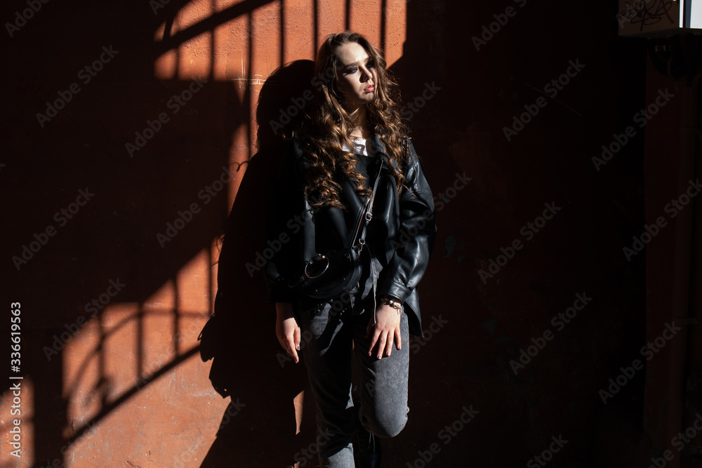 Naklejka premium Outdoor portrait of a young elegant woman in hard light with shadows of urban wearing trendy black jacket with incredible makeup. Close up. Text space.