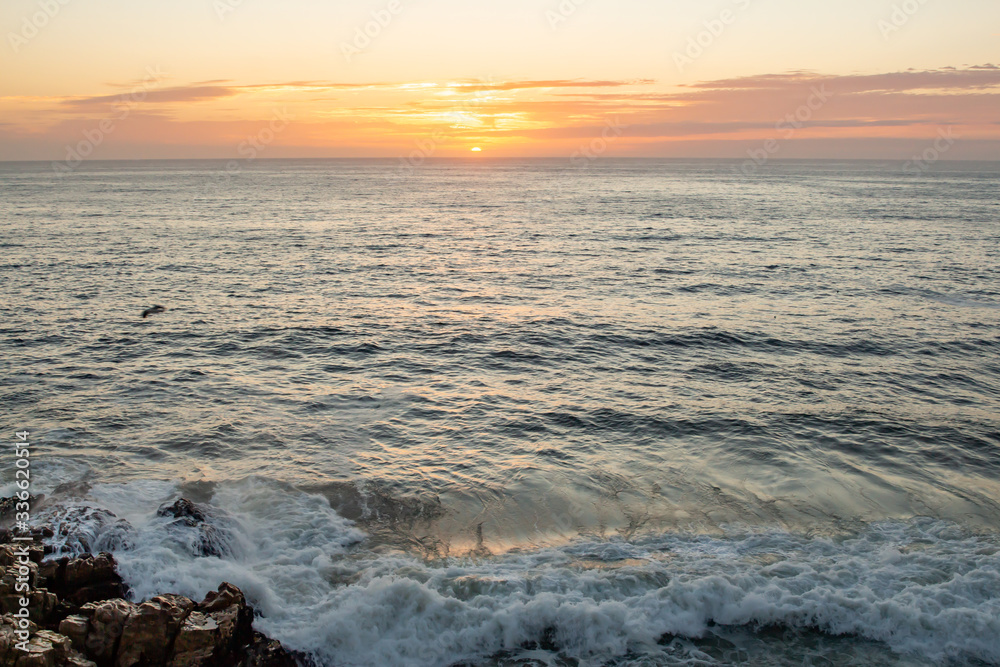 Green hued waves crashing on rocks with beautiful golden clouds at sunrise on the horizon. Green hued waves crashing on rocks with beautiful golden clouds at sunrise on the horizon.