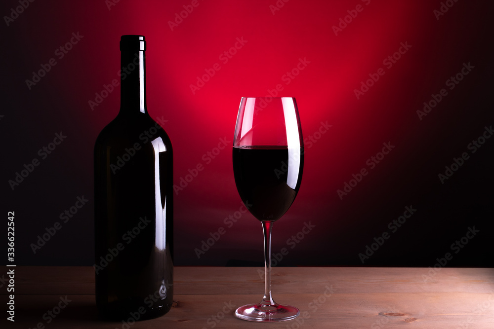 Black bottle of red wine and a glass. A bottle of wine stands on a table, a bottle on a gray background and a wooden table. Red vine.