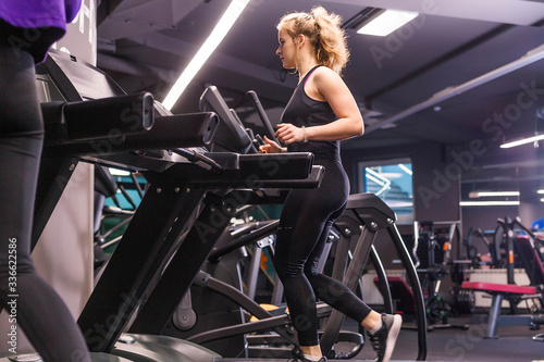 A girl in a black sports uniform runs on a treadmill in a sports hall.