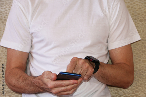 A man in a white T-shirt is watching video on a smartphone.