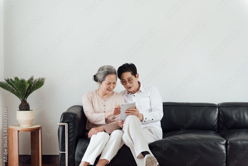 An elderly Asian couple using electronic devices on the sofa An elderly Asian couple using electronic devices on the sofa