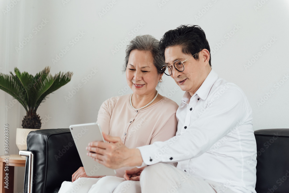 An elderly Asian couple using electronic devices on the sofa An elderly Asian couple using electronic devices on the sofa