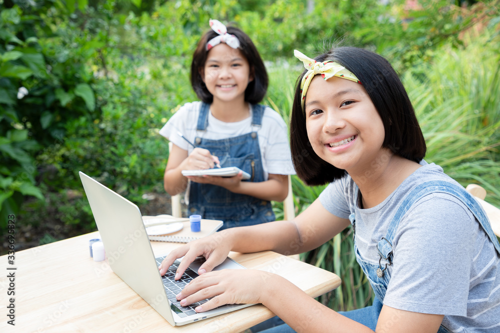 Two little girls are learning through online lessons in the front garden. They were smile and happiness to meet new friends online. Protect coronavirus new strain, or COVID-19. Education from home. Two little girls are learning through online lessons in the front garden. They were smile and happiness to meet new friends online. Protect coronavirus new strain, or COVID-19. Education from home.
