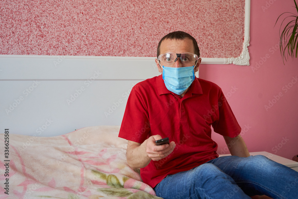 man in medical mask watching television,emotions of a man in a medical mask when watching news at home man in medical mask watching television,emotions of a man in a medical mask when watching news at home