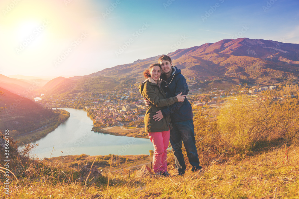 Hugging couple in love stands on the hill with beautiful evening view of mountains valley with Mtskheta city, Kura and Aragvi rivers. Georgia country