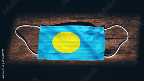 Palau National Flag at medical, surgical, protection mask on black wooden background. Coronavirus Covid–19, Prevent infection, illness or flu. State of Emergency, Lockdown photo