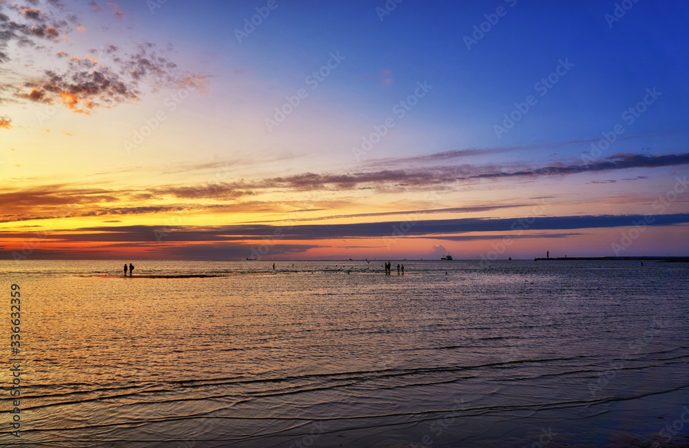 Beautiful sunset on the Baltic Sea with people, passenger ship and lighthouse in the background.