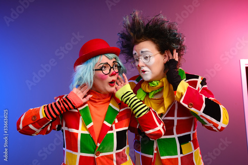 Two clowns a man and a woman with makeup in bright colored costumes are fooling around and showing a presentation