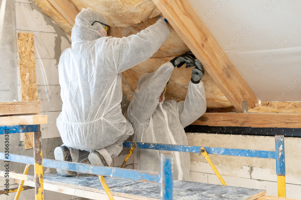 Foreman in overalls working with rockwool insulation material - obrazy, fototapety, plakaty 