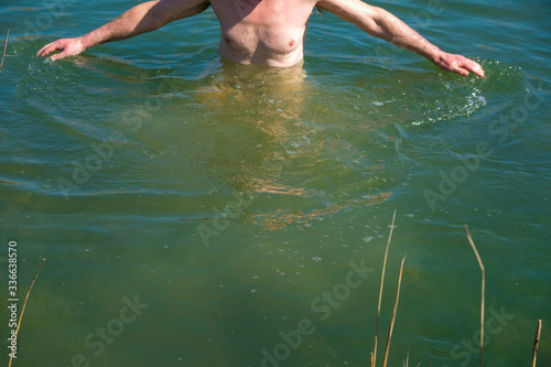Fototapeta Naklejka Na Ścianę i Meble -  Isolated man stands waist-deep in Aqua Menthe water in Ukraine. Hands wide apart. Part of body without head. Copy space.