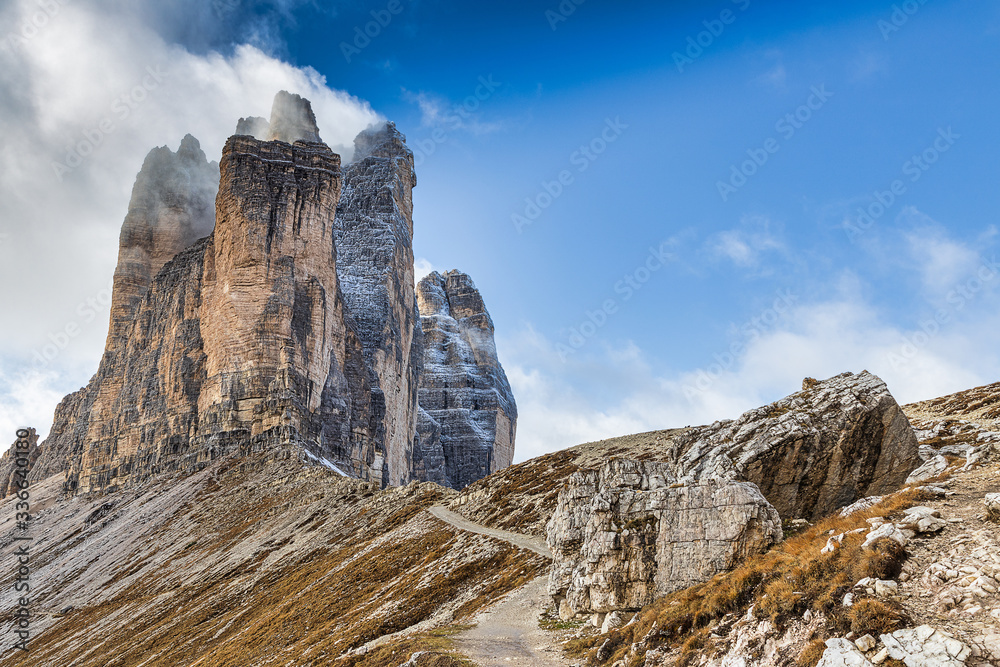 Fototapeta premium Hiking trail with a view of amazing Tre Cime di Lavaredo mountains covered with snow in autumn, Dolomites, Italy