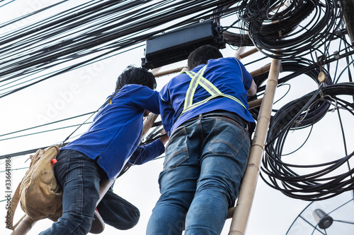 Electrical linemam worker climb a bamboo ladder to repair wire. A telecom engineer installing wire for internet. © phoderstock