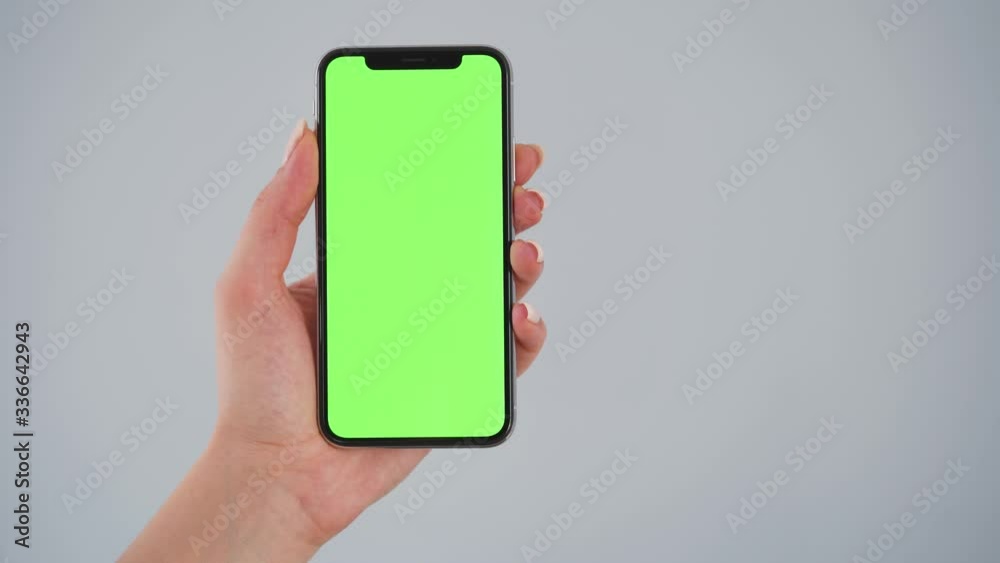 Female hands holding a smartphone with a green screen on a gray background. Chroma key. Copy Space