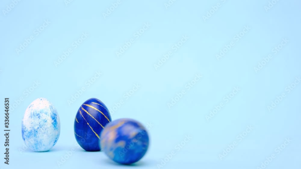 Easter eggs are rolling, knocking each other on blue table. Eggs trendy colored classic blue, white and golden . Happy Easter. Minimal style Easter eggs are rolling, knocking each other on blue table. Eggs trendy colored classic blue, white and golden . Happy Easter. Minimal style