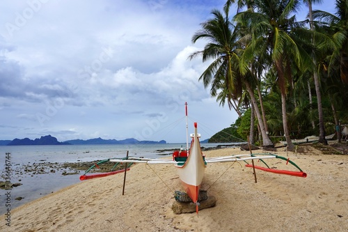 Typical filipino boat parked at the sandy beach in clear turquoise sea water - it is real paradise scenery