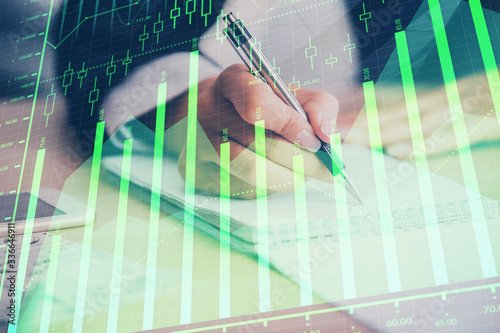 A woman hands writing information about stock market in notepad. Forex chart holograms in front. Concept of research. Multi exposure